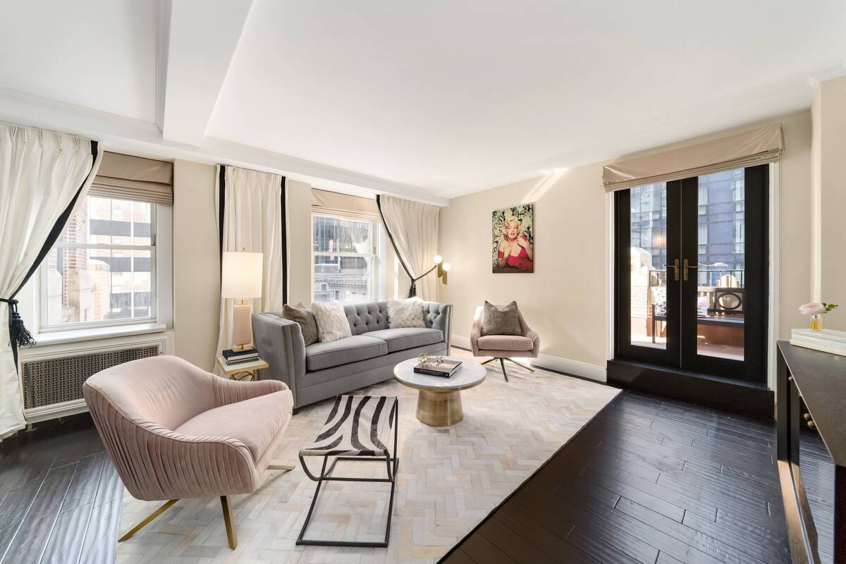 A modern living room with a grey sofa, a pink armchair, a round coffee table, and a black and white rug.