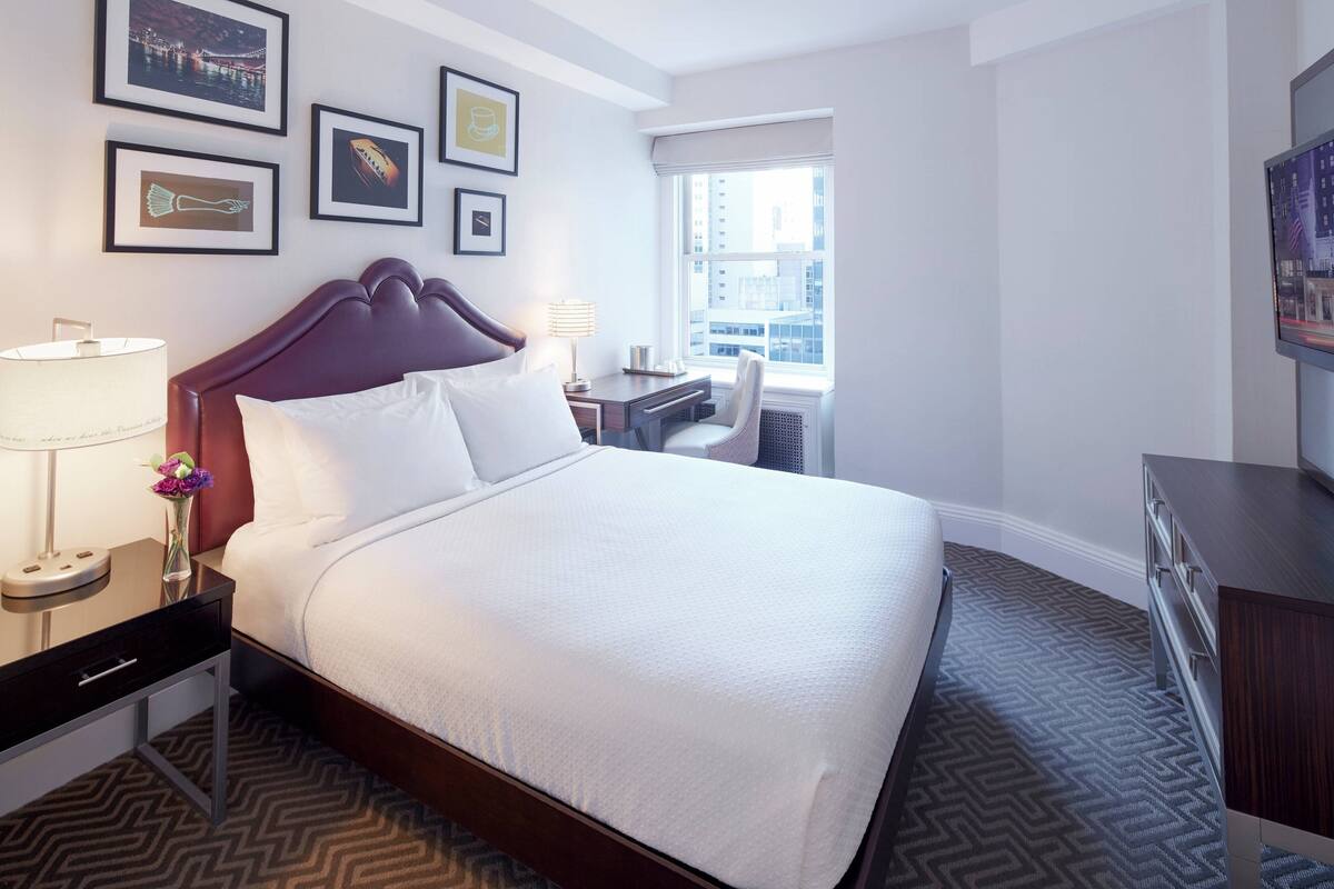 A hotel room with a large bed, a desk, a chair, and a TV.