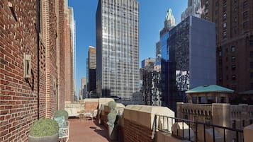 A rooftop terrace with a brick wall, a modern glass building, and a historic building with a green roof.