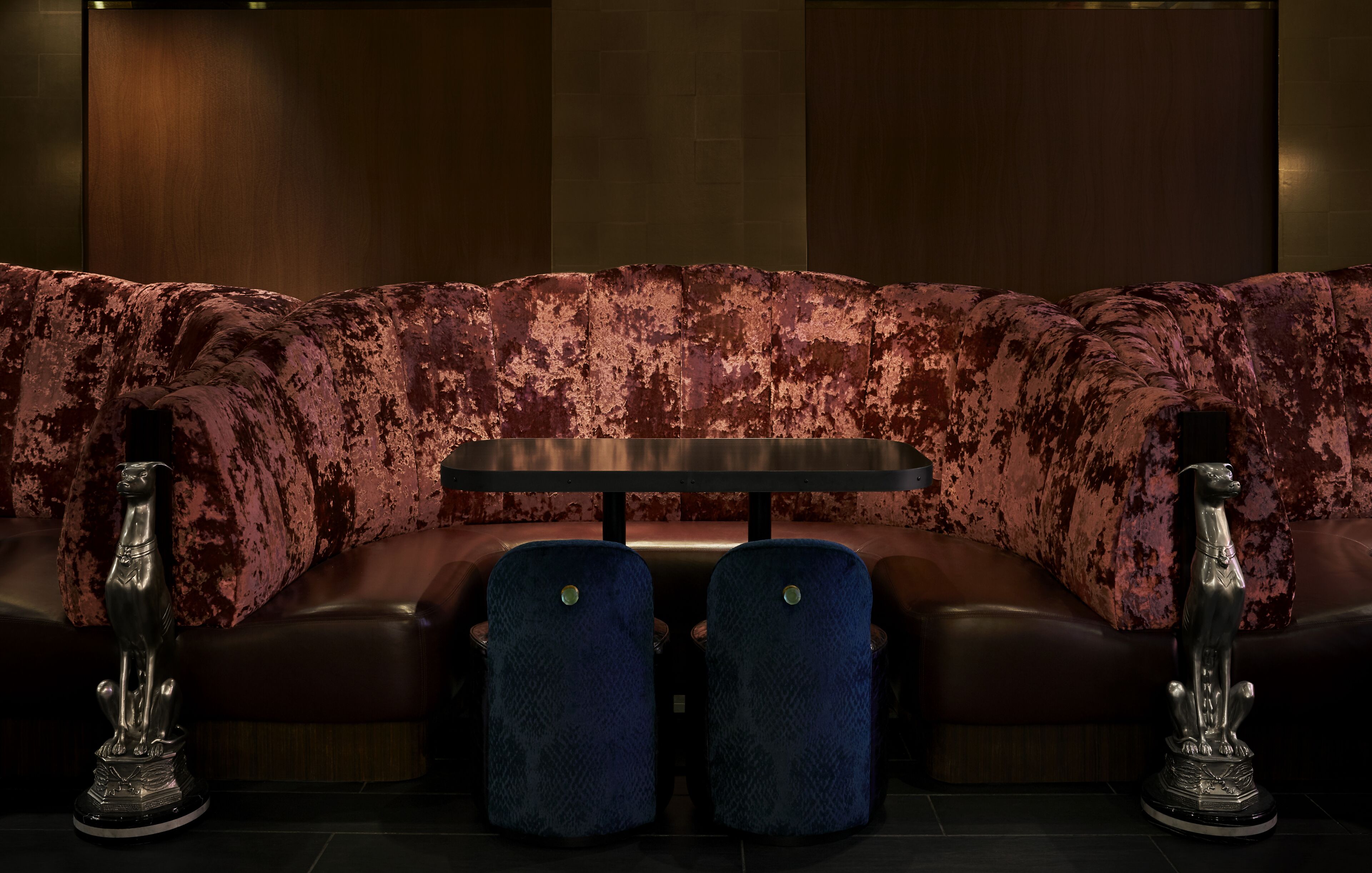 A dark red velvet sofa with a small table and two blue upholstered chairs in front.