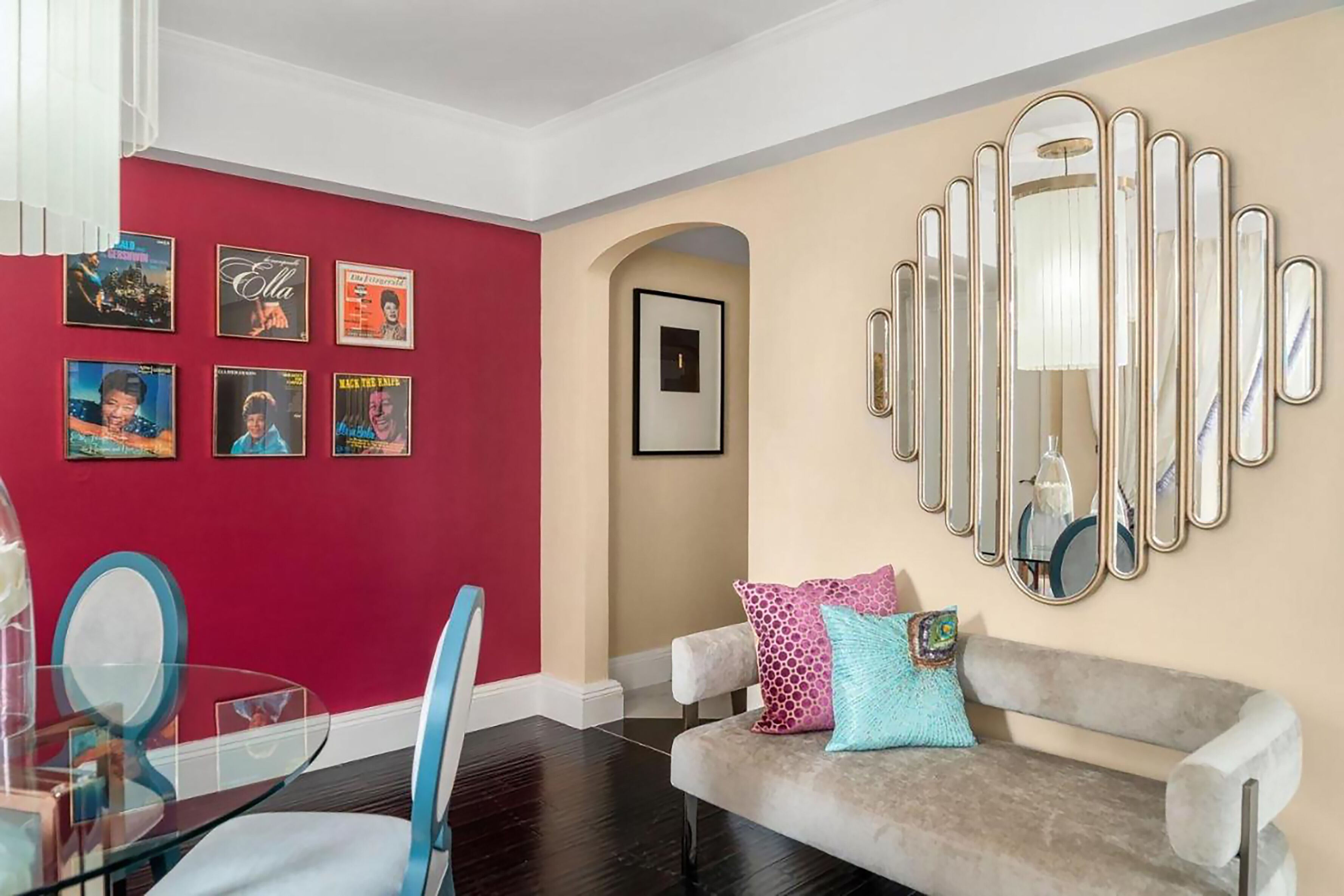 A living room with a red wall, a beige wall, a glass table, a grey sofa, and a large mirror.