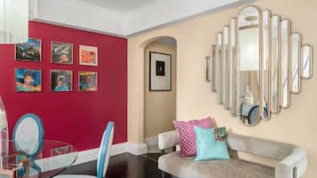 A living room with a red wall, a beige wall, a glass table, a grey sofa, and a large mirror.