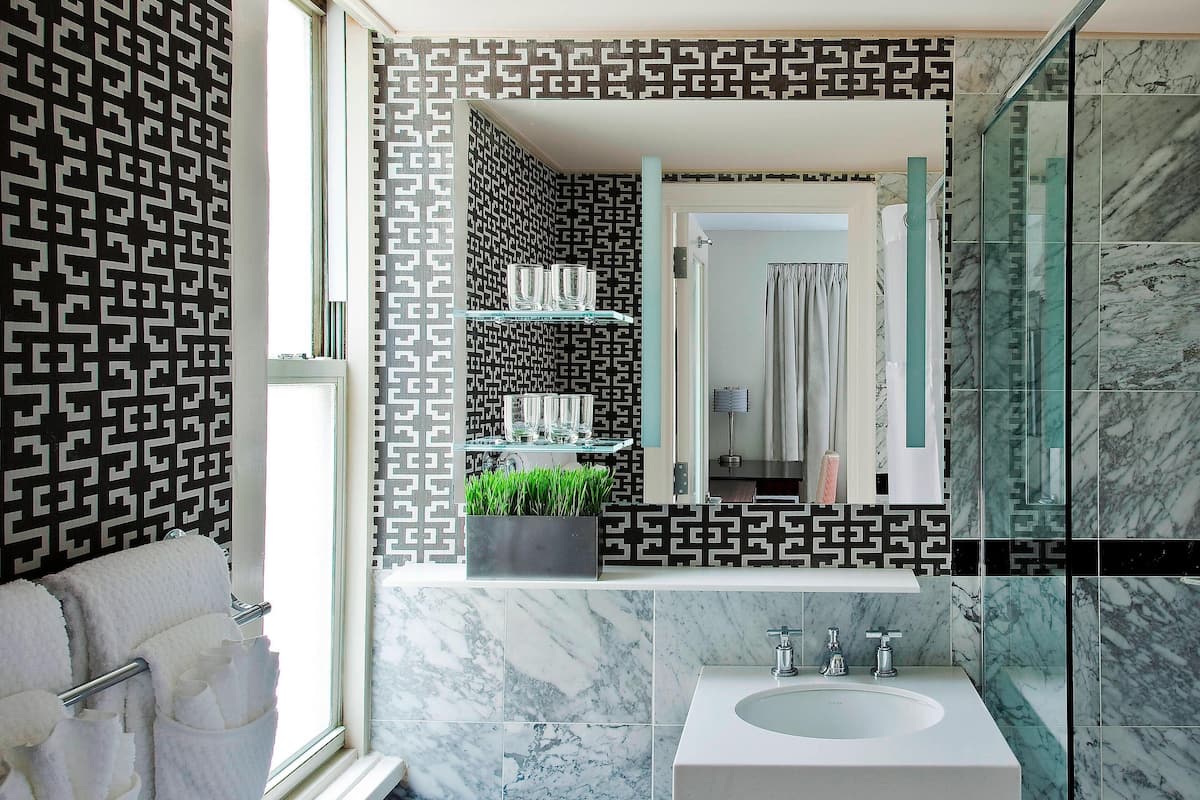 Un baño moderno con lavamanos de mármol, estantes de vidrio y pared con diseño.