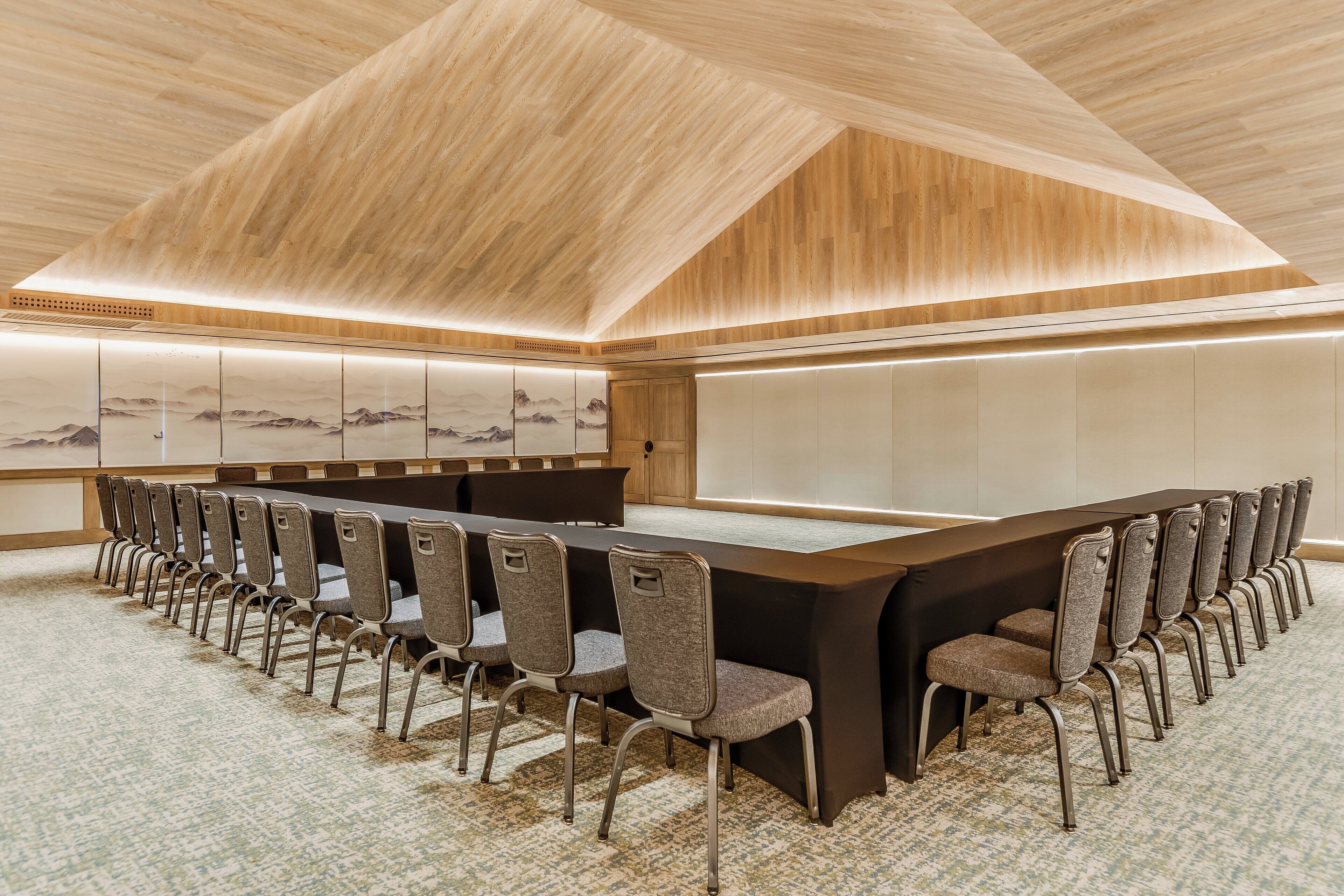 Un salón de conferencias con una larga mesa y sillas, techo de madera y una obra de arte colgada en la pared.