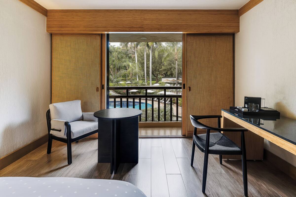 A hotel room with a balcony, a sofa, a small round table, a desk, and a bed.