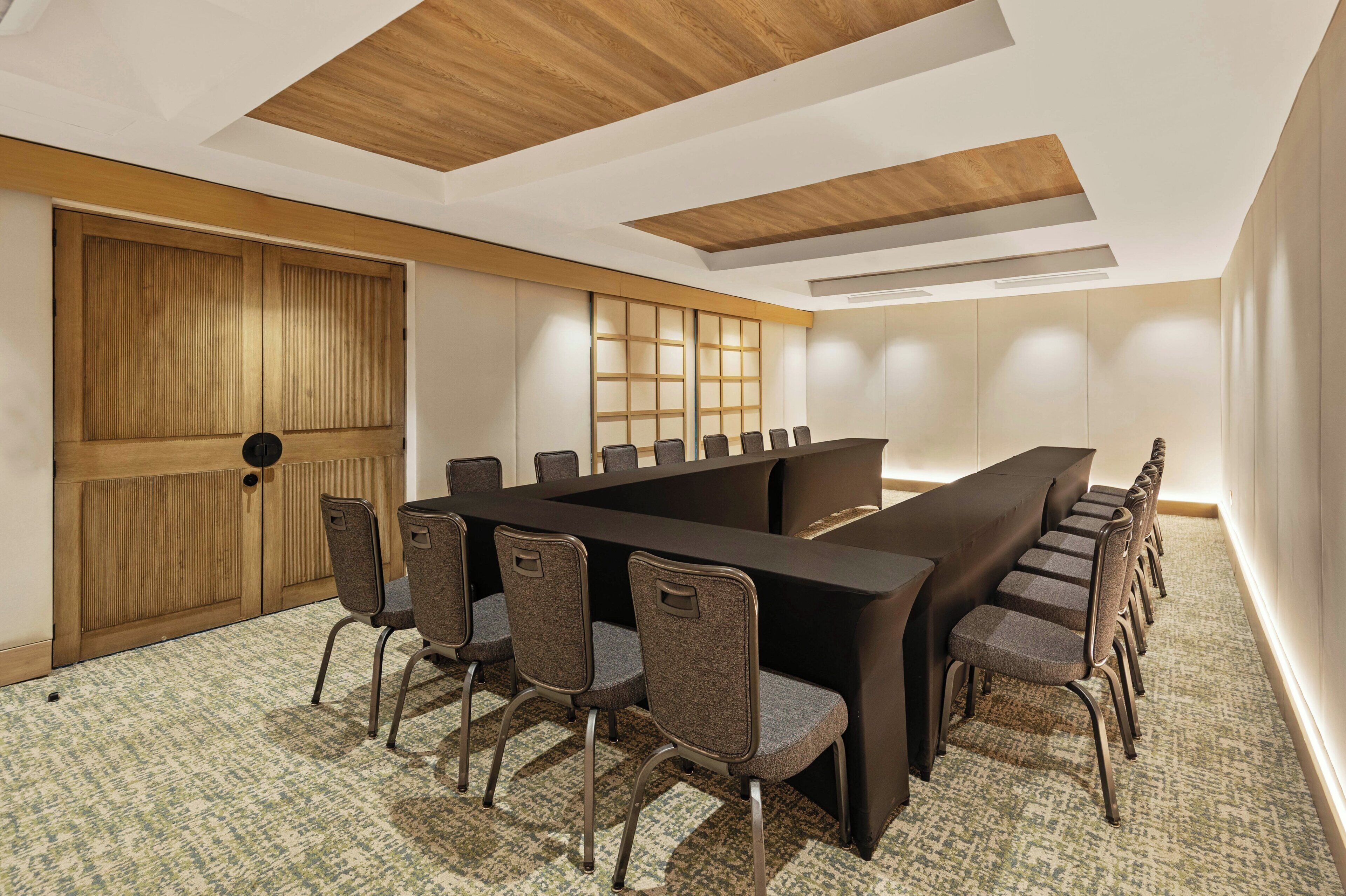 A conference room with a long table, chairs, wooden paneling, and a patterned carpet.