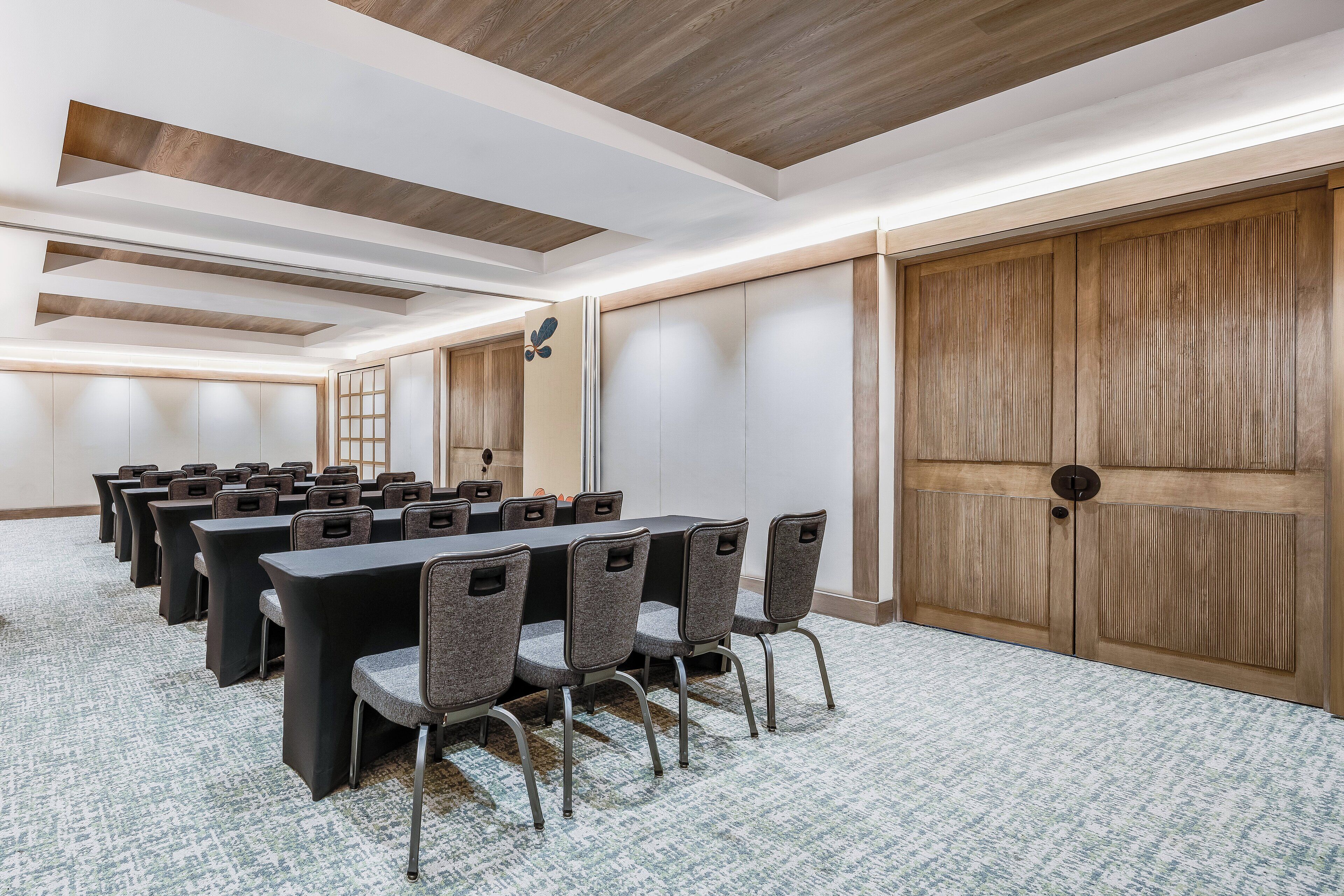 Una sala conferenze con un lungo tavolo, diverse sedie e una porta di legno.