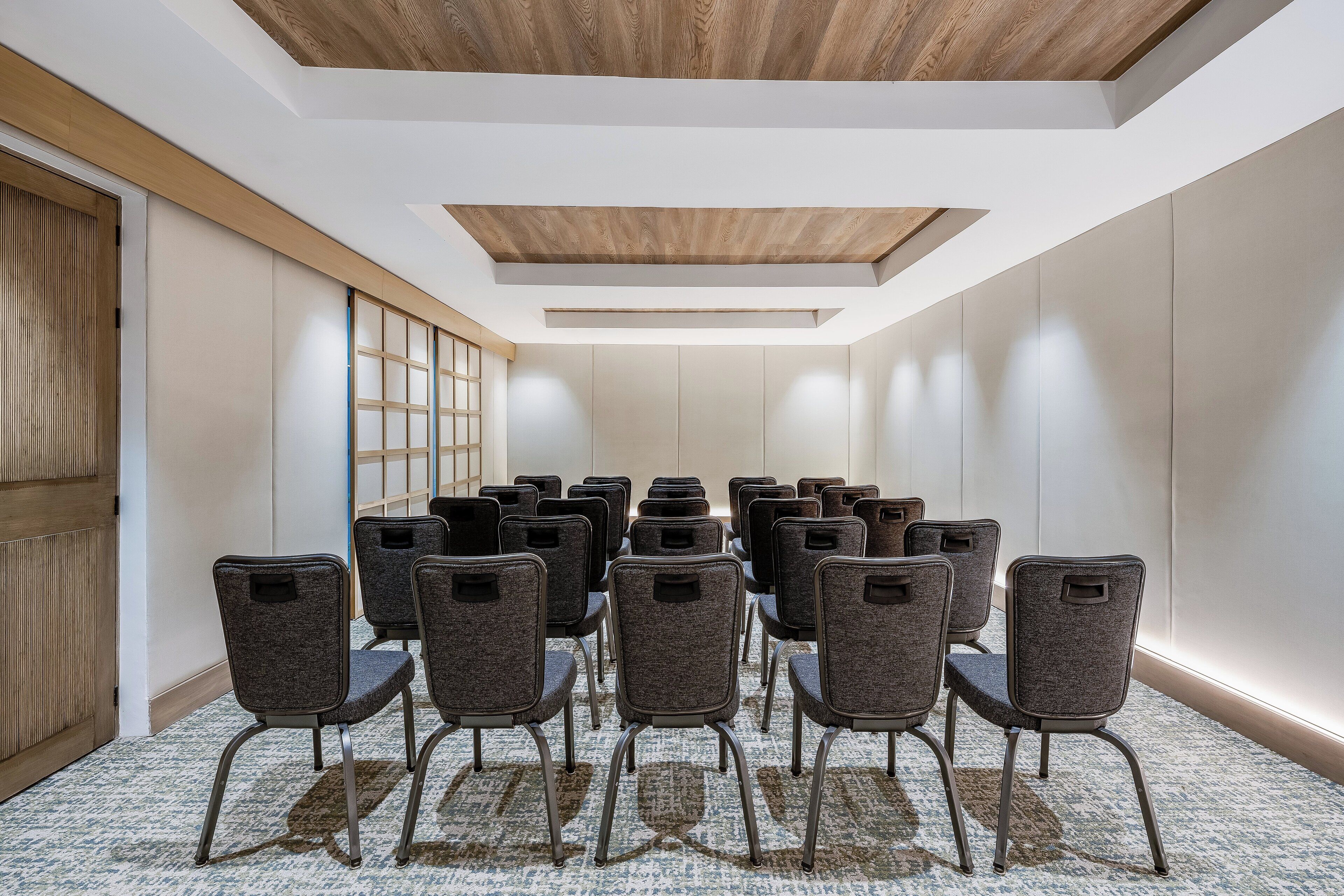 Un salón de conferencias con filas de sillas, techo de madera y un amplio ventanal con persianas.