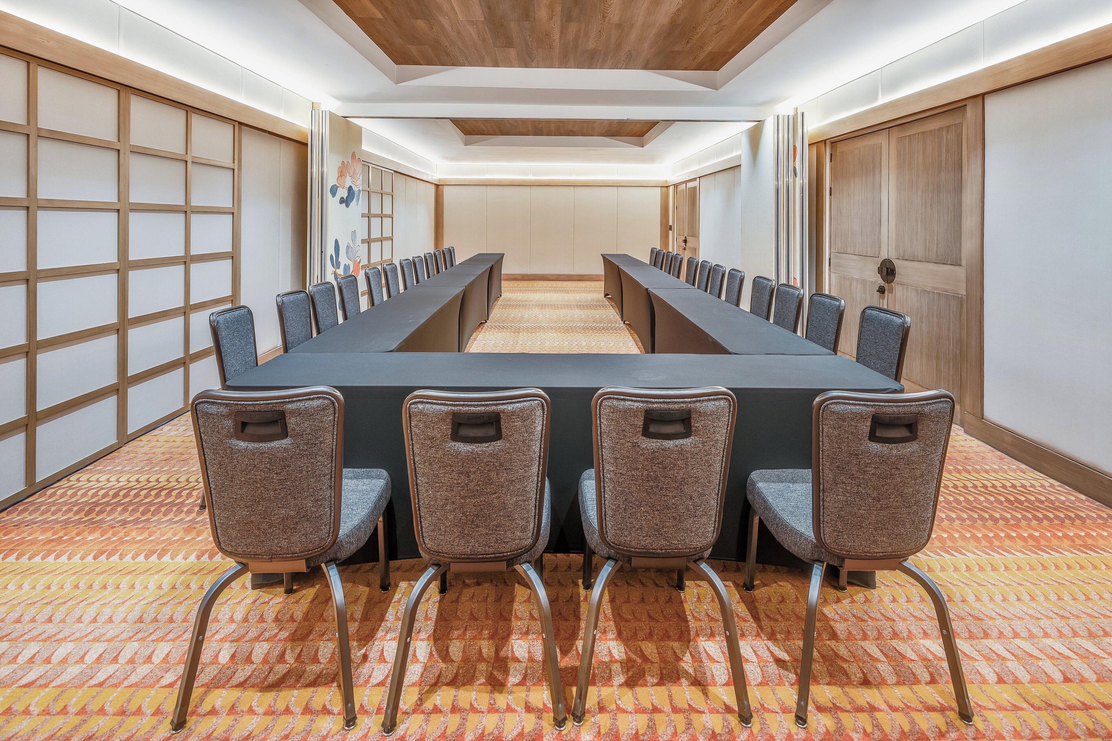 A conference room with a long table, four chairs, and a patterned carpet.