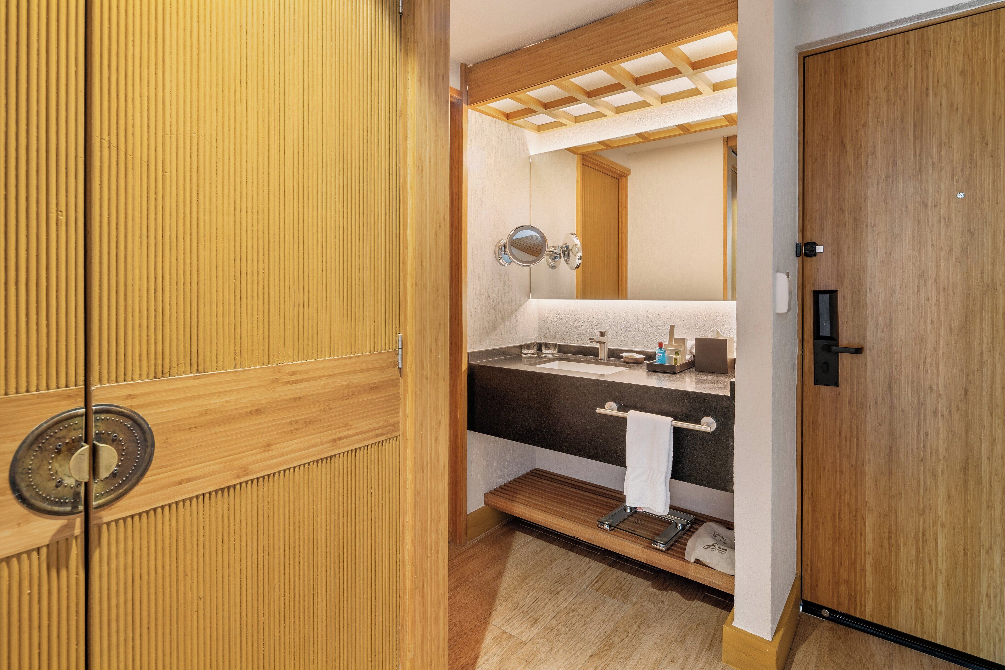 A bathroom with a wooden door, a sink with a mirror, and a towel rack.
