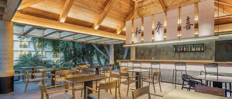 A spacious outdoor dining area with wooden tables and chairs, a bar with bottles, and a wooden ceiling structure.
