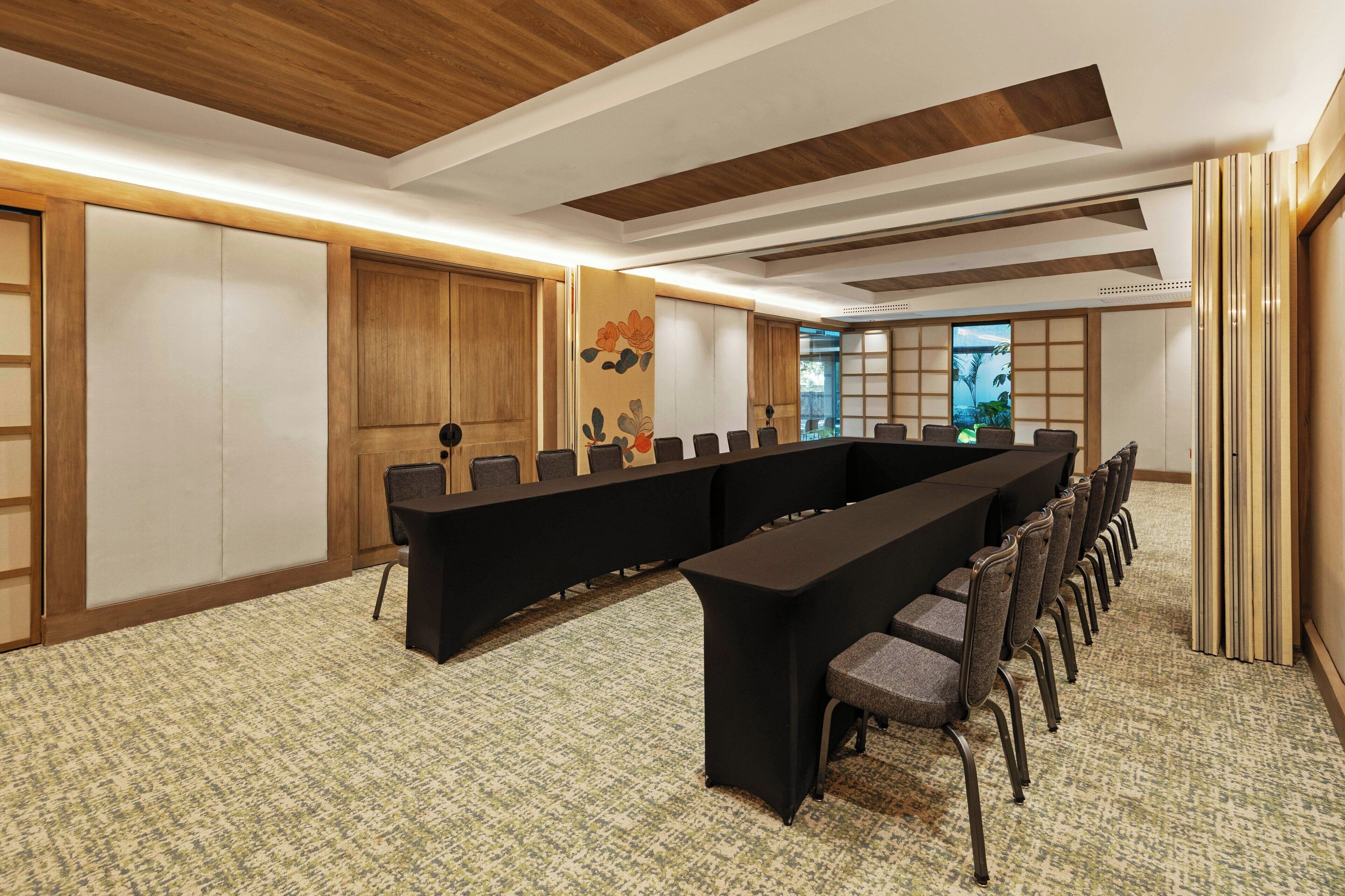 Une salle de conférence avec une longue table et des chaises, des panneaux de bois et un tapis à motifs.
