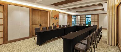 Une salle de conférence avec une longue table et des chaises, des panneaux de bois et un tapis à motifs.