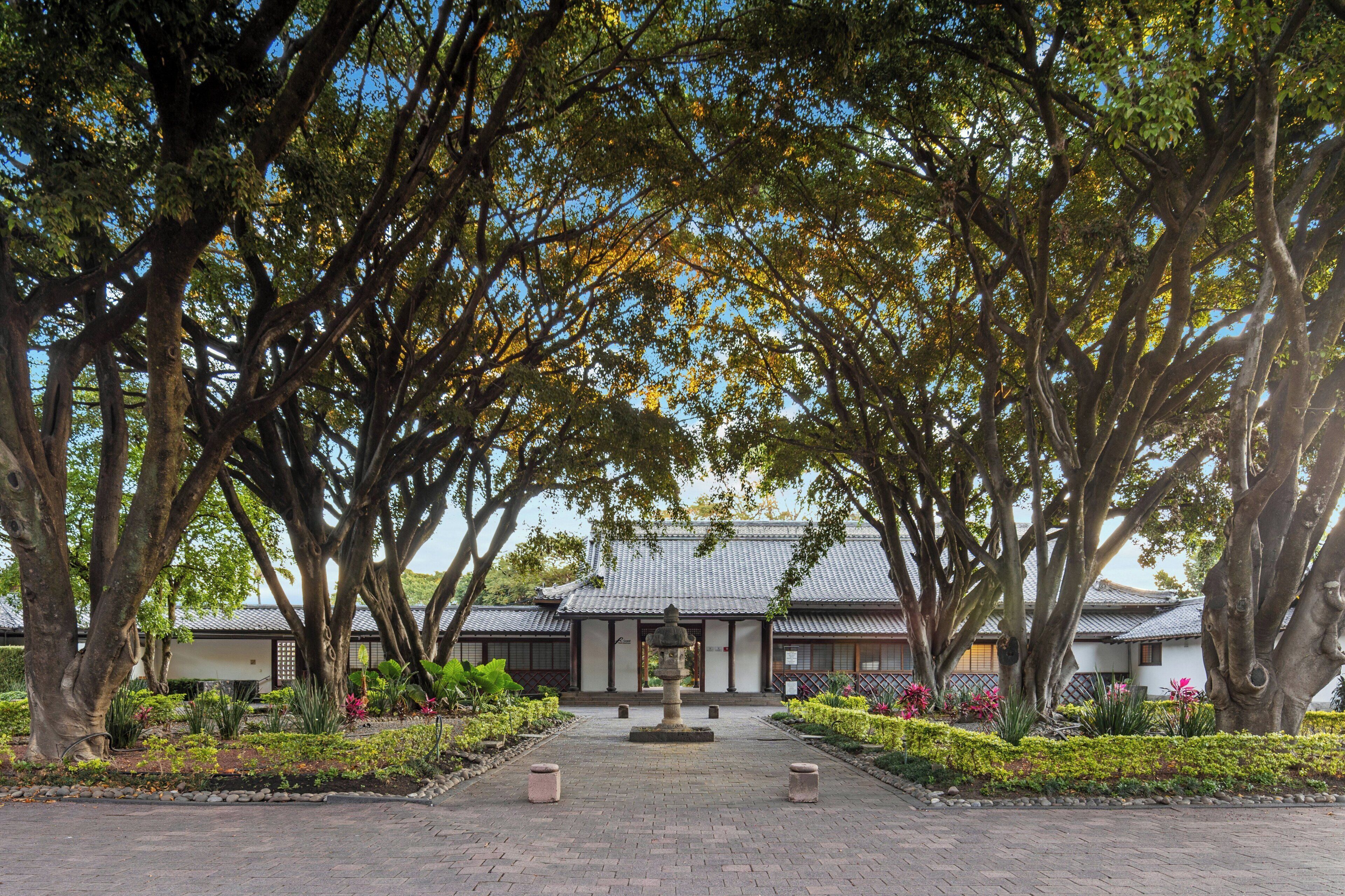 A traditional building with a tiled roof, surrounded by a garden with various plants and a central stone structure.