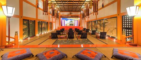 A traditional room with tatami mats, a stage with a backdrop, and a row of chairs facing the stage.