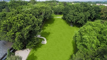 Vista aérea de un parque con un césped central, rodeado de árboles frondosos y un sendero que atraviesa la vegetación.