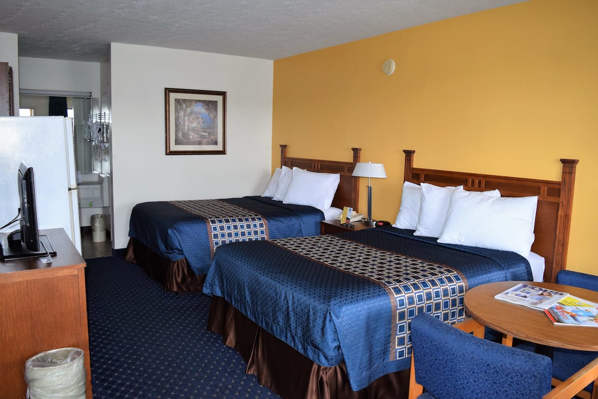 A hotel room with two beds, a desk, a chair, a table, and a trash bin.