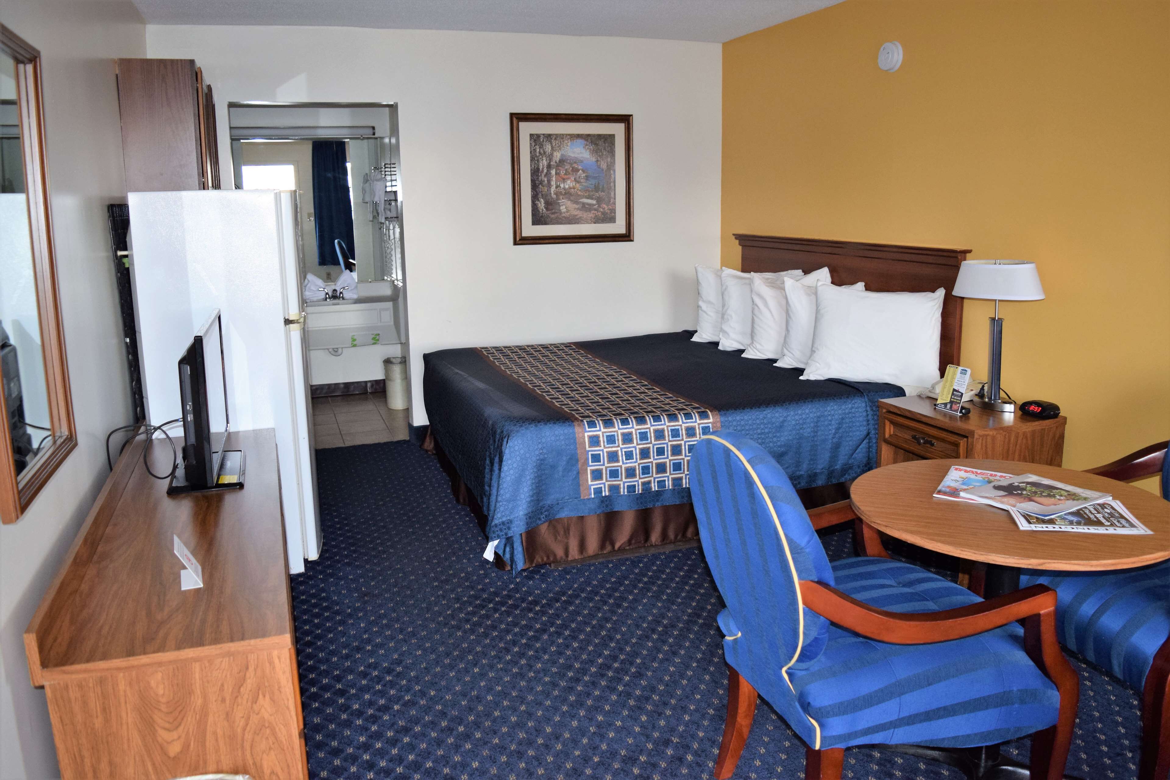 Une chambre d’hôtel avec un lit, un bureau avec un ordinateur, une chaise, une table avec un magazine et un tableau au mur.