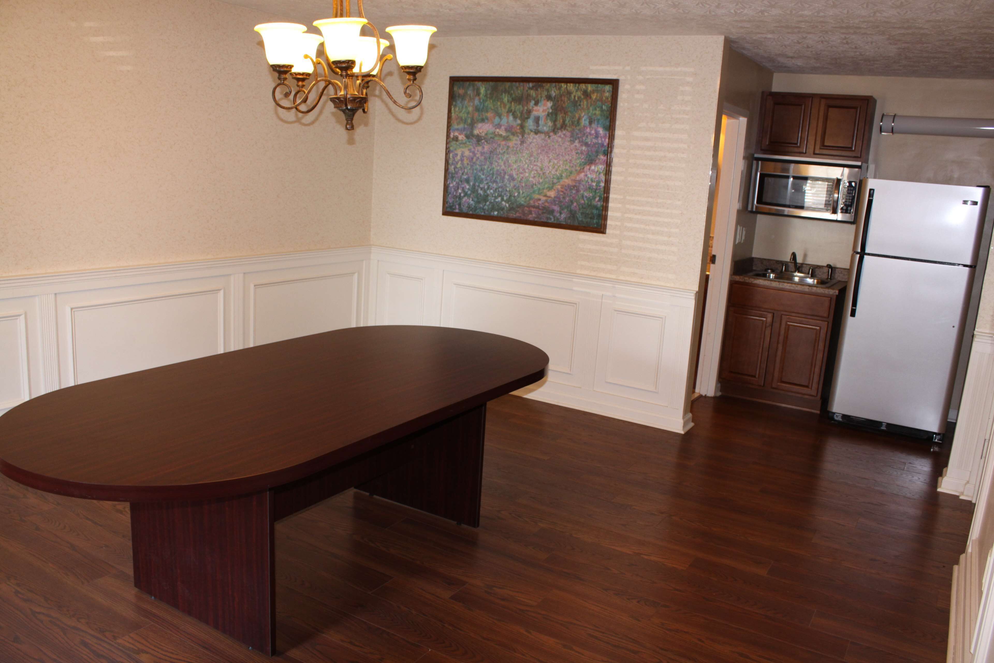A kitchen with a wooden table, white cabinetry, a painting, and modern appliances.