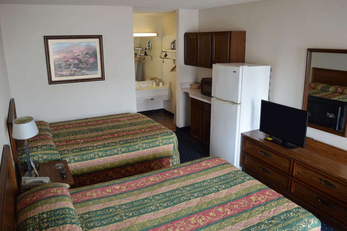 A hotel room with two beds, a television, a refrigerator, a sink, and a cabinet.