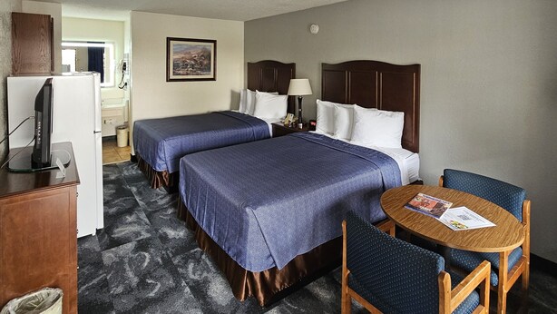 A hotel room with two beds, a desk with a computer, a chair, and a small table with a magazine.