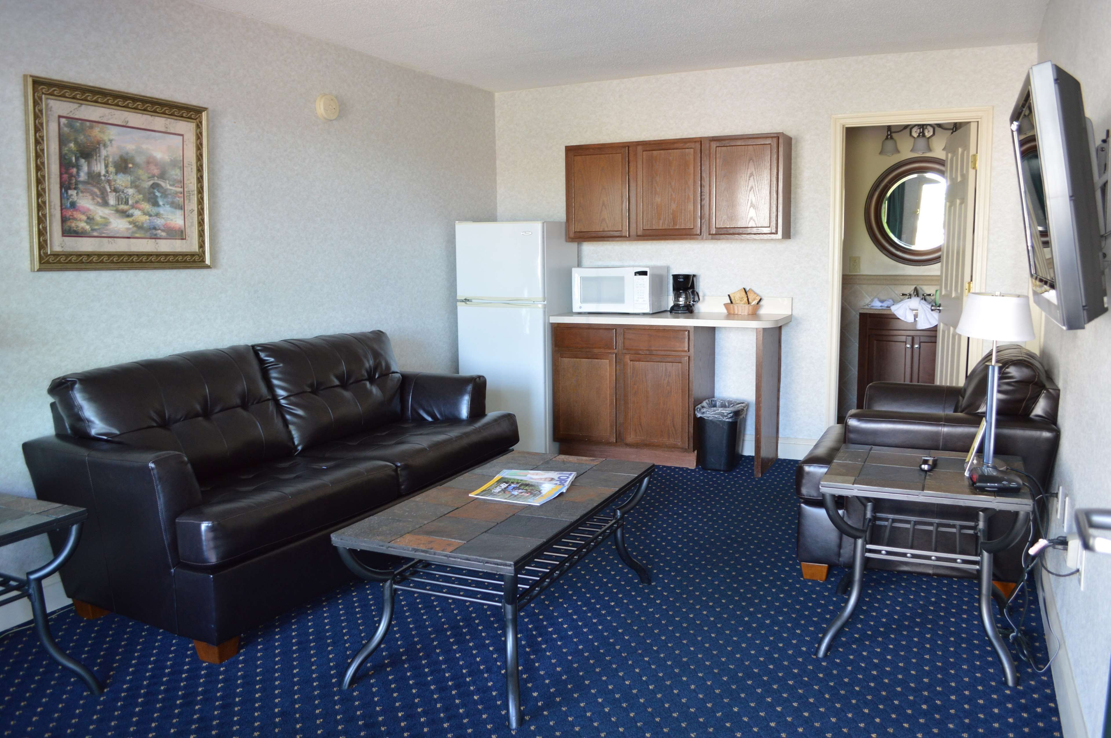 A compact living space with a black leather sofa, a small kitchenette with a microwave, and a television mounted on the wall.