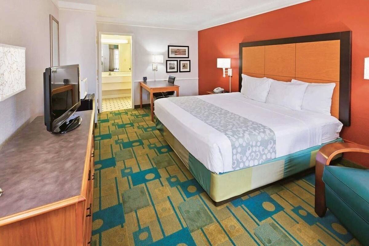Une chambre d’hôtel avec un lit, un bureau, une télévision et une salle de bain que l’on aperçoit à l’arrière-plan.