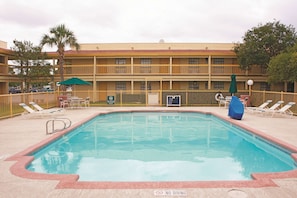 Un espace piscine d’hôtel avec des chaises longues, des parasols et un panneau indiquant qu’il est interdit de plonger.
