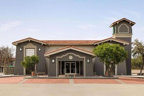 A two-story building with a central entrance, a clock tower, and a red-tiled roof. - La Quinta Inn By Wyndham IH-10 West San Antonio TX (San Antonio)