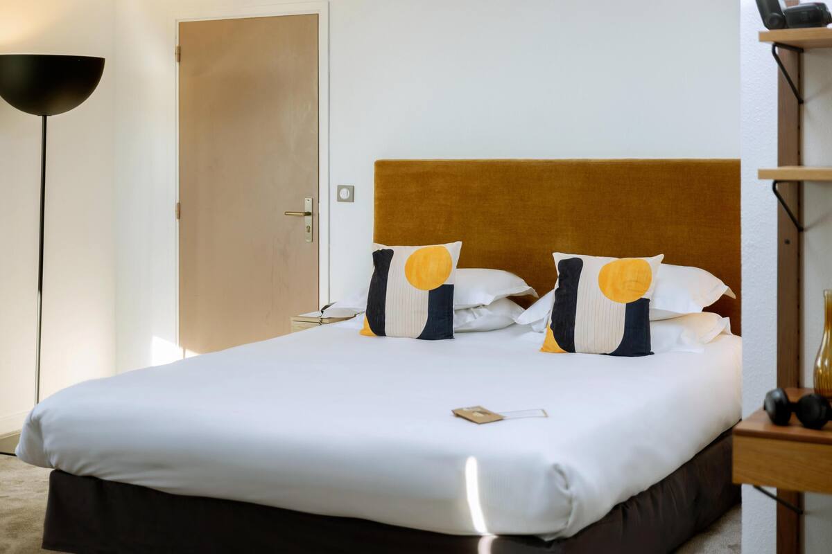 Una habitación de hotel con una cama grande, una mesita de noche, una lámpara y una puerta.