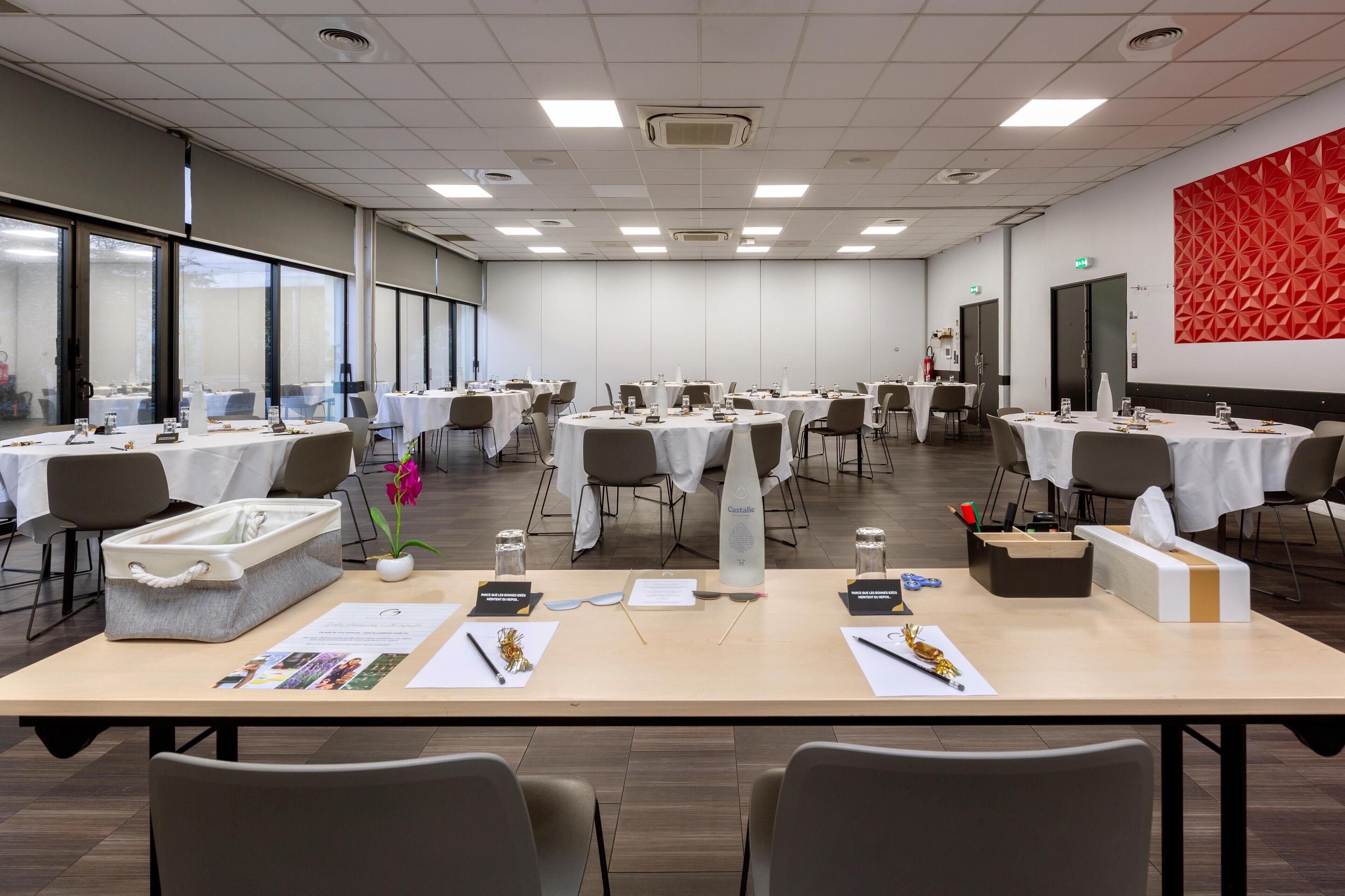Une salle de conférence équipée de tables rondes, de chaises et d’une grande décoration murale géométrique rouge.