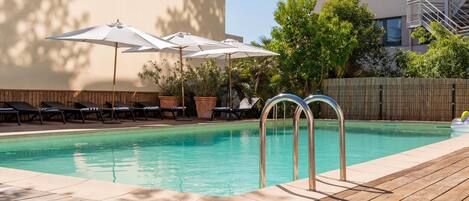 A swimming pool with lounge chairs and umbrellas, surrounded by a wooden deck and a building.