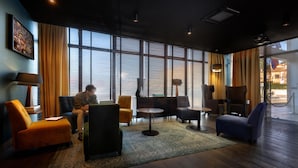 Un moderno hall de hotel con un gran ventanal, un sofá, sillones, una mesita y una lámpara.