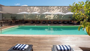 Una piscina con sillas de descanso y sombrillas, rodeada por una terraza de madera y un muro bajo.