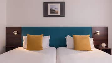 Una cama doble con almohadas blancas y mostaza, un cabecero verde azulado y un cuadro enmarcado encima.