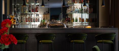 A bar area with multiple shelves of bottles, a bar counter, and green bar stools.