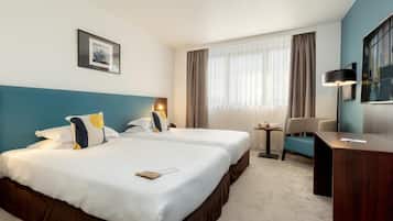 A hotel room with two beds, a desk, a chair, a lamp, a framed picture, and a large window with curtains.