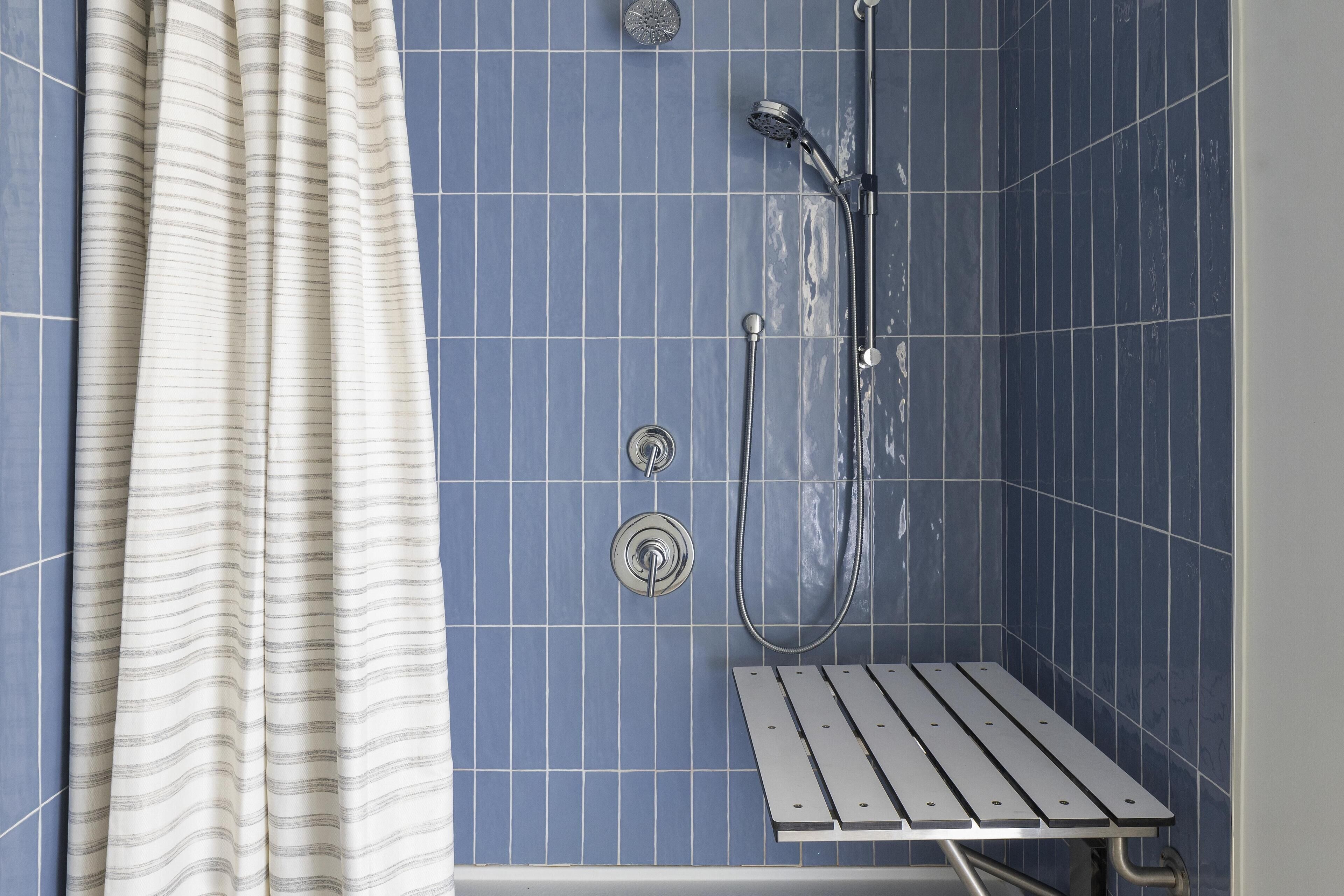 A shower area with blue tiles, a showerhead, and a metal bench.