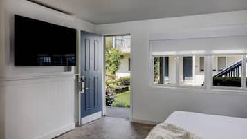 Une chambre dotée d’une grande télévision, d’une porte donnant sur un balcon et d’une fenêtre offrant une vue sur l’extérieur.