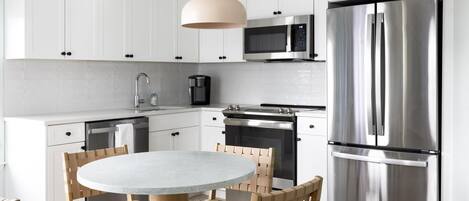 A modern kitchen with white cabinets, stainless steel appliances, a round table, and woven chairs.
