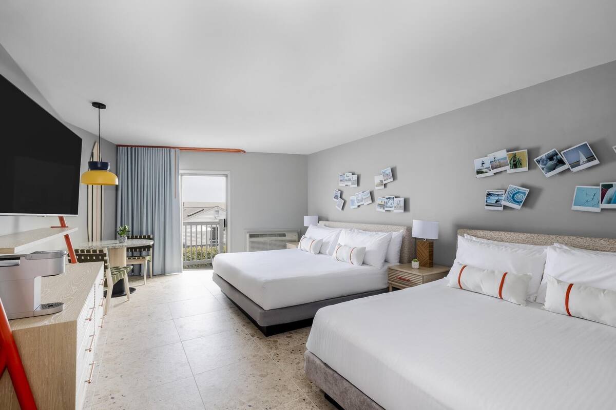 A hotel room with two beds, a desk, a TV, and a balcony with a view.