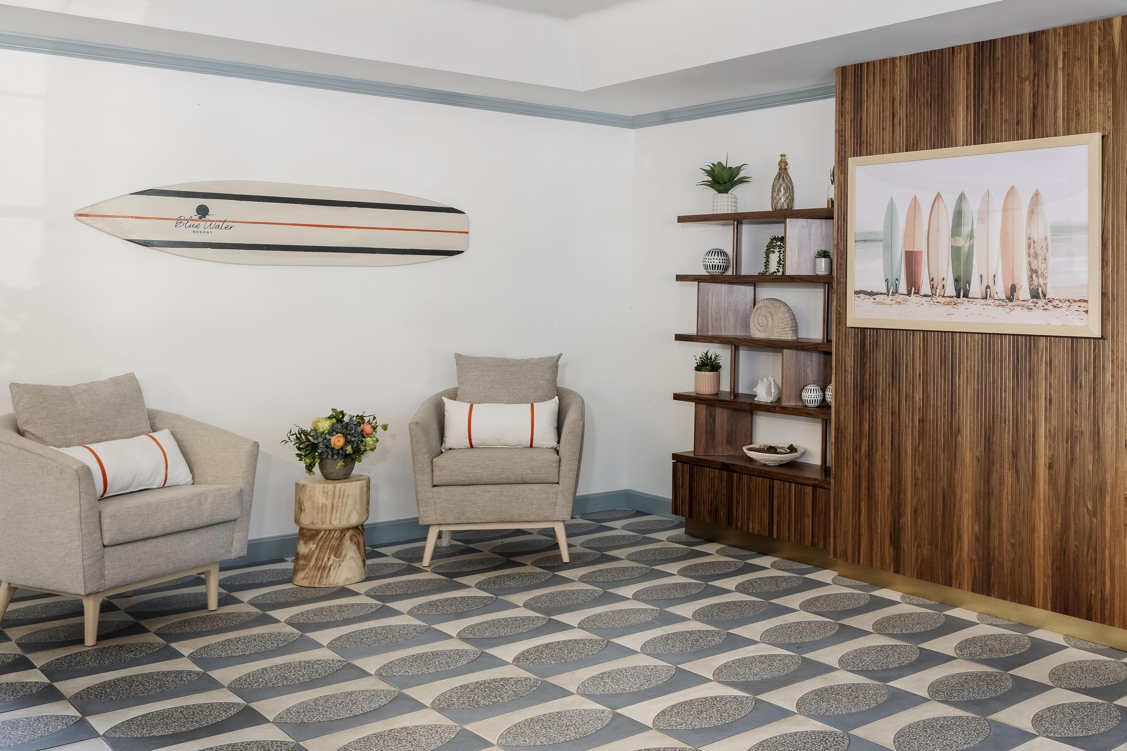 Ein Zimmer mit zwei Sesseln, einer Holzkommode, einem Surfbrett an der Wand und einem gerahmten Bild von Surfbrettern.