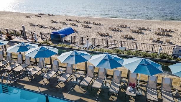 A pool area with lounge chairs and umbrellas, a beach with sun loungers, and a clear view of the ocean. - Blue Water Resort (South Yarmouth)