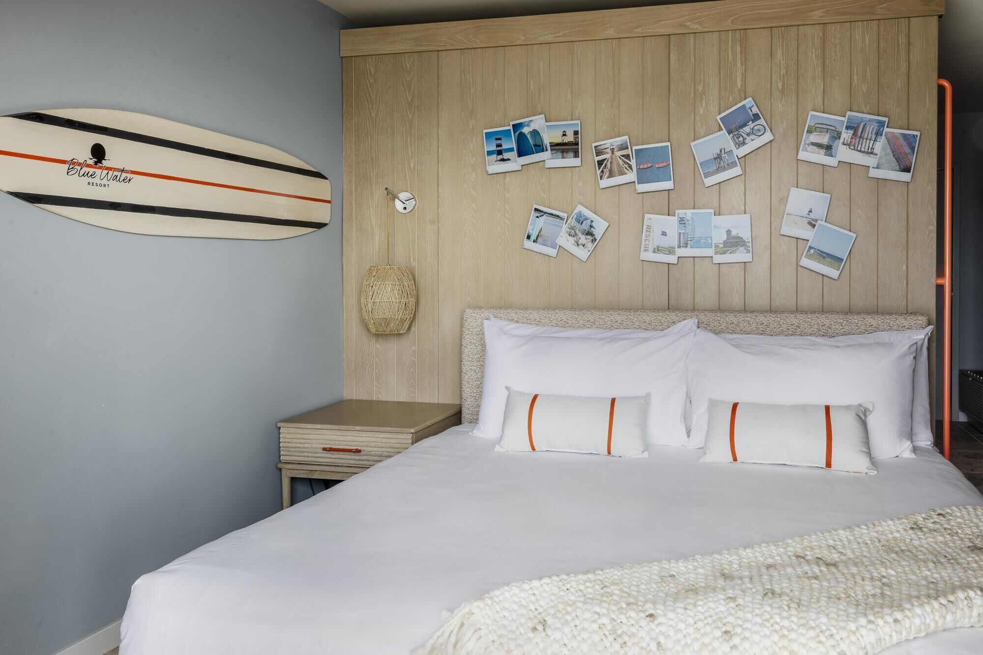A bedroom with a bed, a nightstand, a wall-mounted clock, and a surfboard.