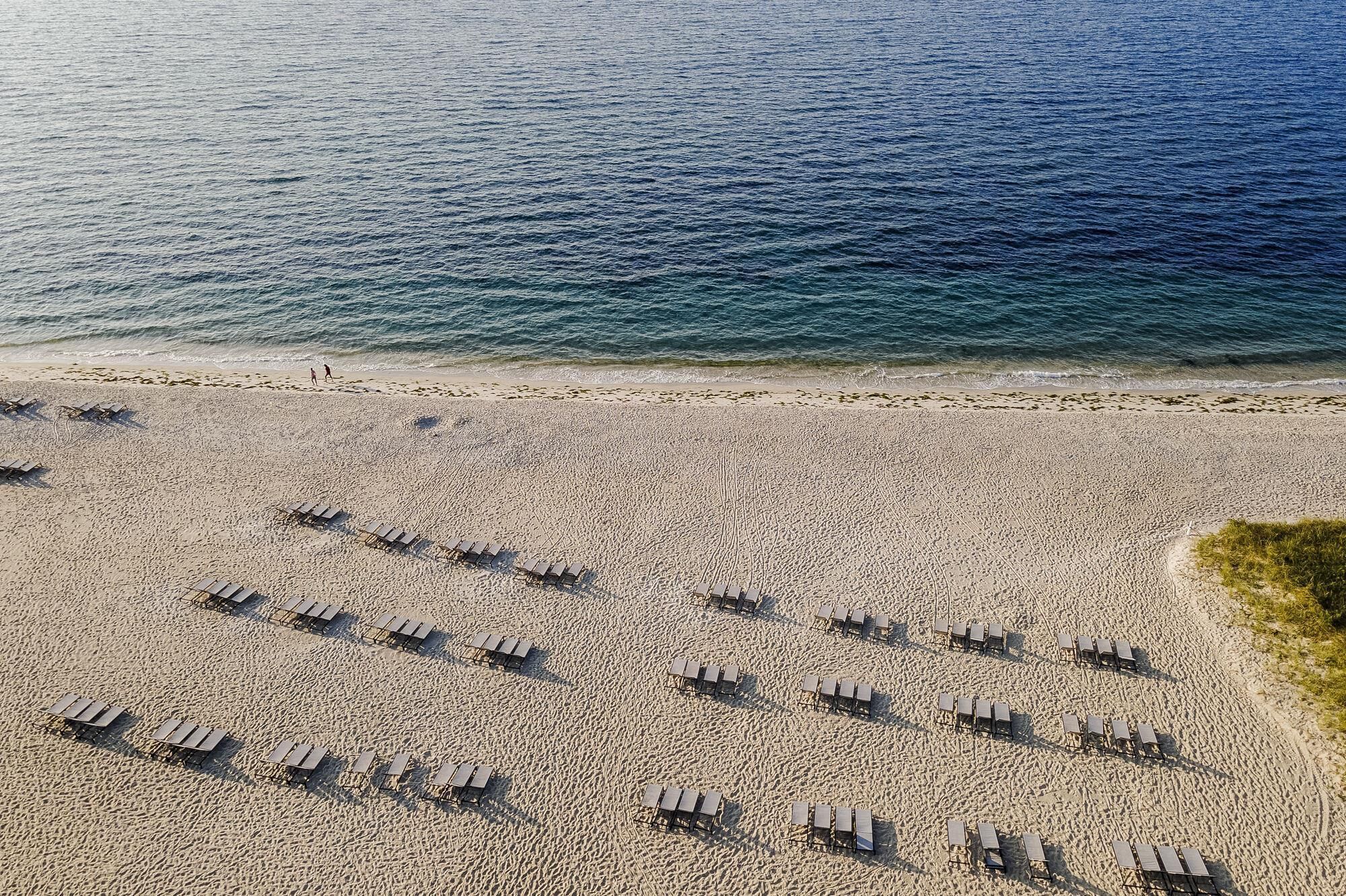 Een luchtbeeld van een strand met rijen ligbedden parallel aan de waterlijn.