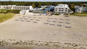 A beach with rows of sun loungers and a building complex in the background. - Blue Water Resort (South Yarmouth)