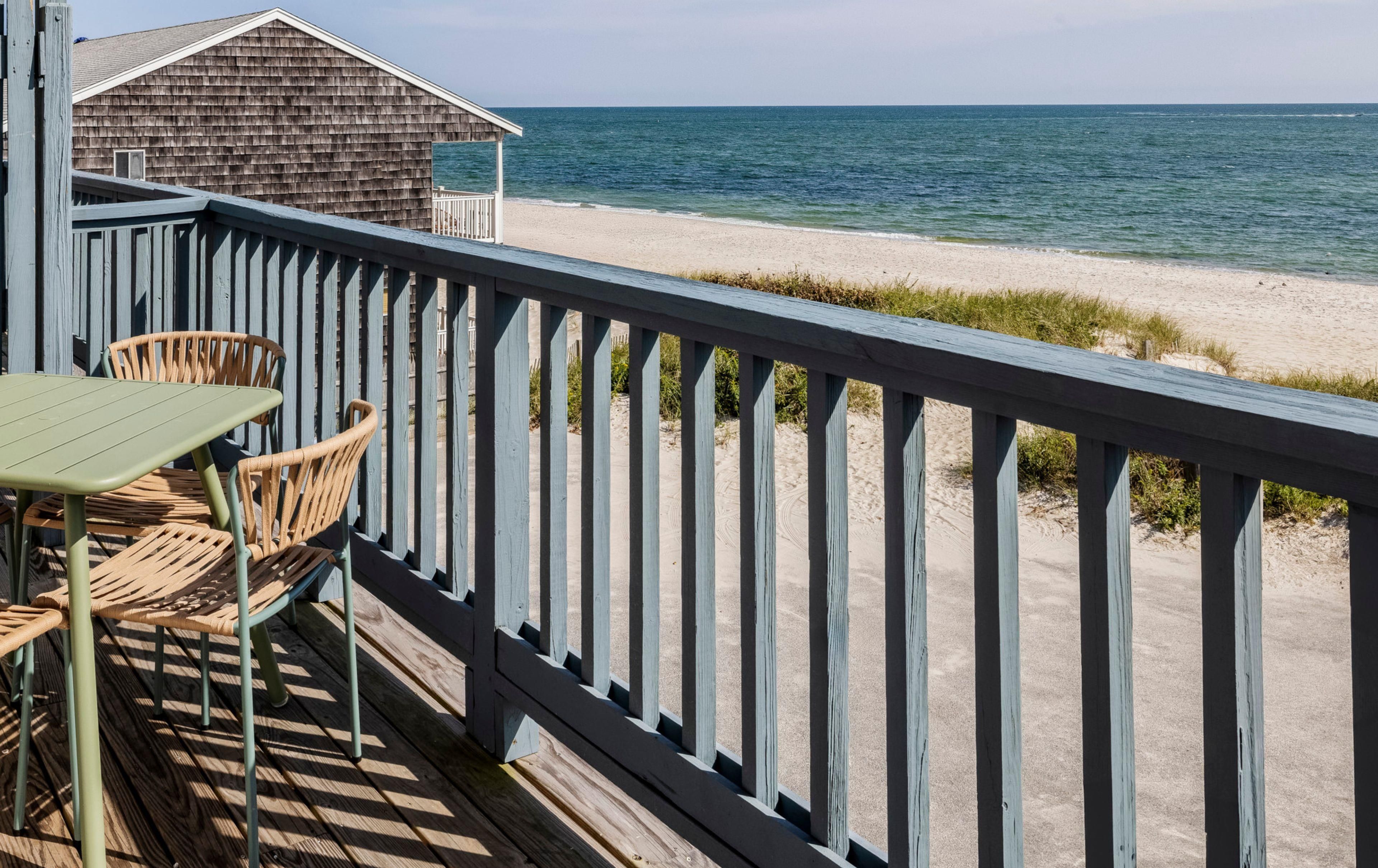 Une terrasse en bois avec une table et des chaises donnant sur une plage.
