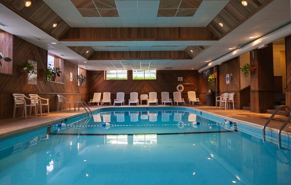 An indoor swimming pool with clear water, surrounded by white lounge chairs and wooden walls.