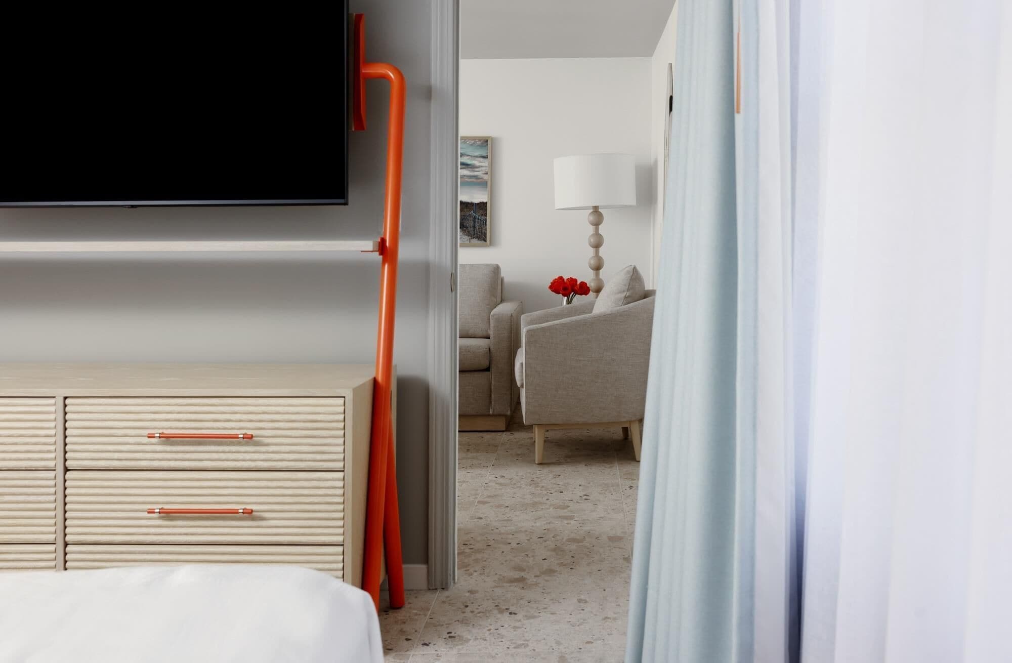 A hotel room with a bed, a TV, a desk with drawers, a chair, a lamp, and a painting on the wall.