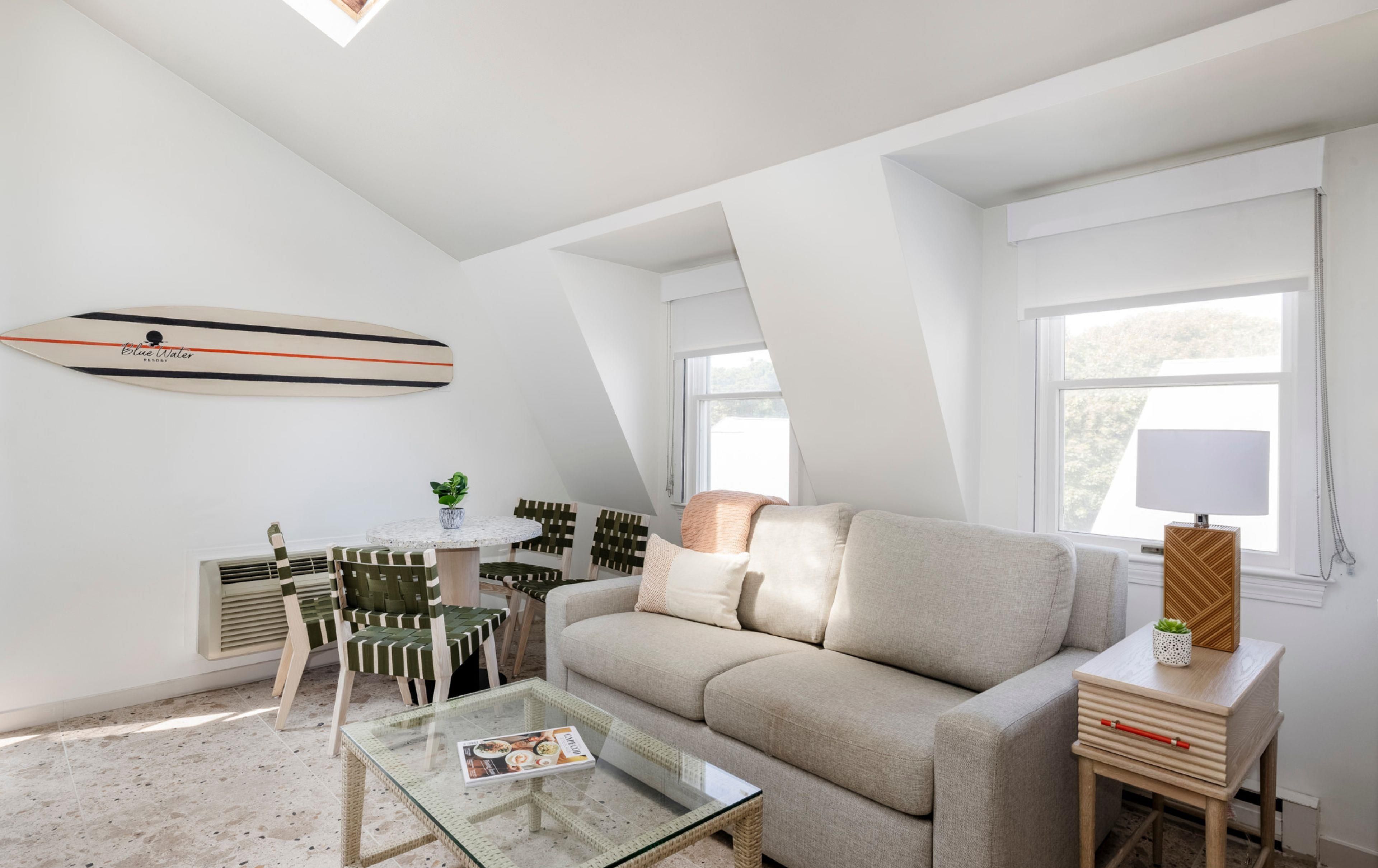 A modern living room with a glass coffee table, a sofa, and a dining area with chairs.